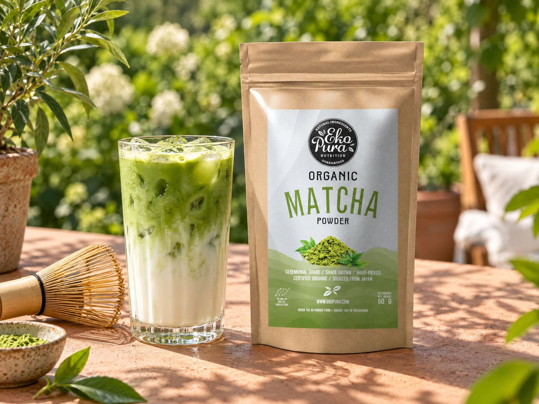 Iced matcha latte in un bicchiere con ghiaccio, accanto a Ekopura Matcha in polvere biologico e a una frusta di bambù