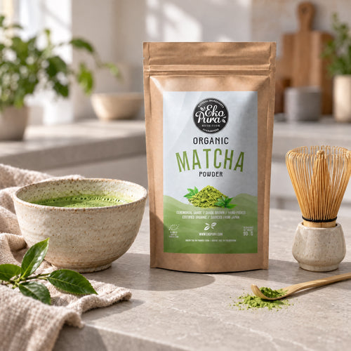 Ekopura Organic Matcha Powder on a light grey stone kitchen counter, with a bowl of matcha, a bamboo whisk and a bamboo scoop